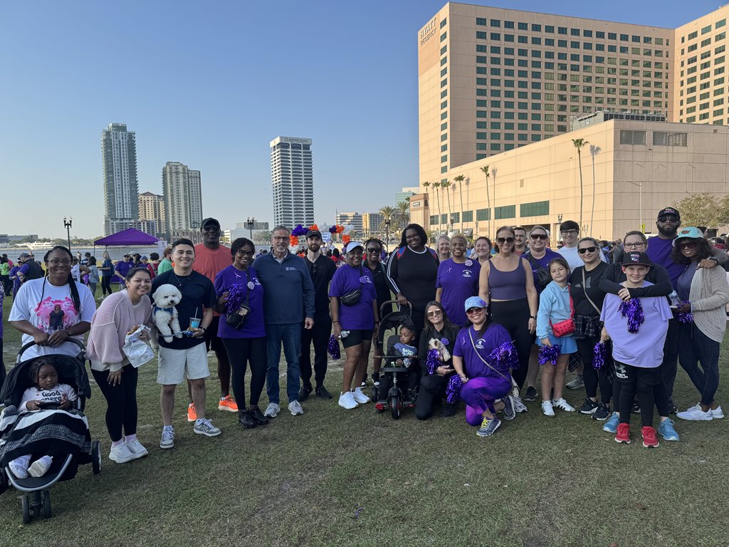 Photo of Clerk team members assembled before the event with Clerk Phillips. They are standing on a grassy field with the skyline of Jacksonville behind them